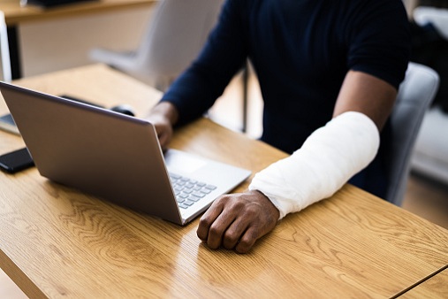 Injured Worker Compensation. Broken Arm African Man On Computer